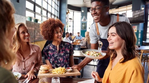 Waiter Serving Group Of Female Friends Meeting For Drinks And Food In Restaurant